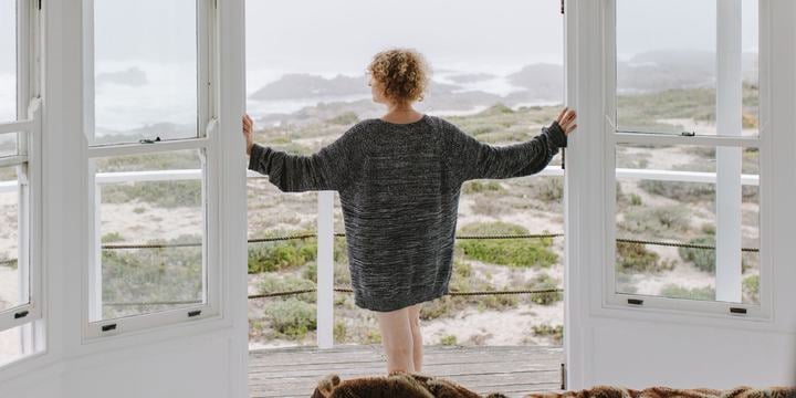 A woman stands in a beach house looking out to the water